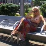 Smiling blonde with huge breasts topless on bench