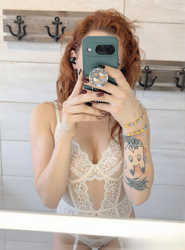 hotwife pics - Who’s the Hotwife Behind the Phone? A hotwife's mirror selfie reveals a woman in a white lace bodysuit, nipples faintly visible, with red curls and a playful tattoo. Captured in a bathroom sett... - Hotwife Pics